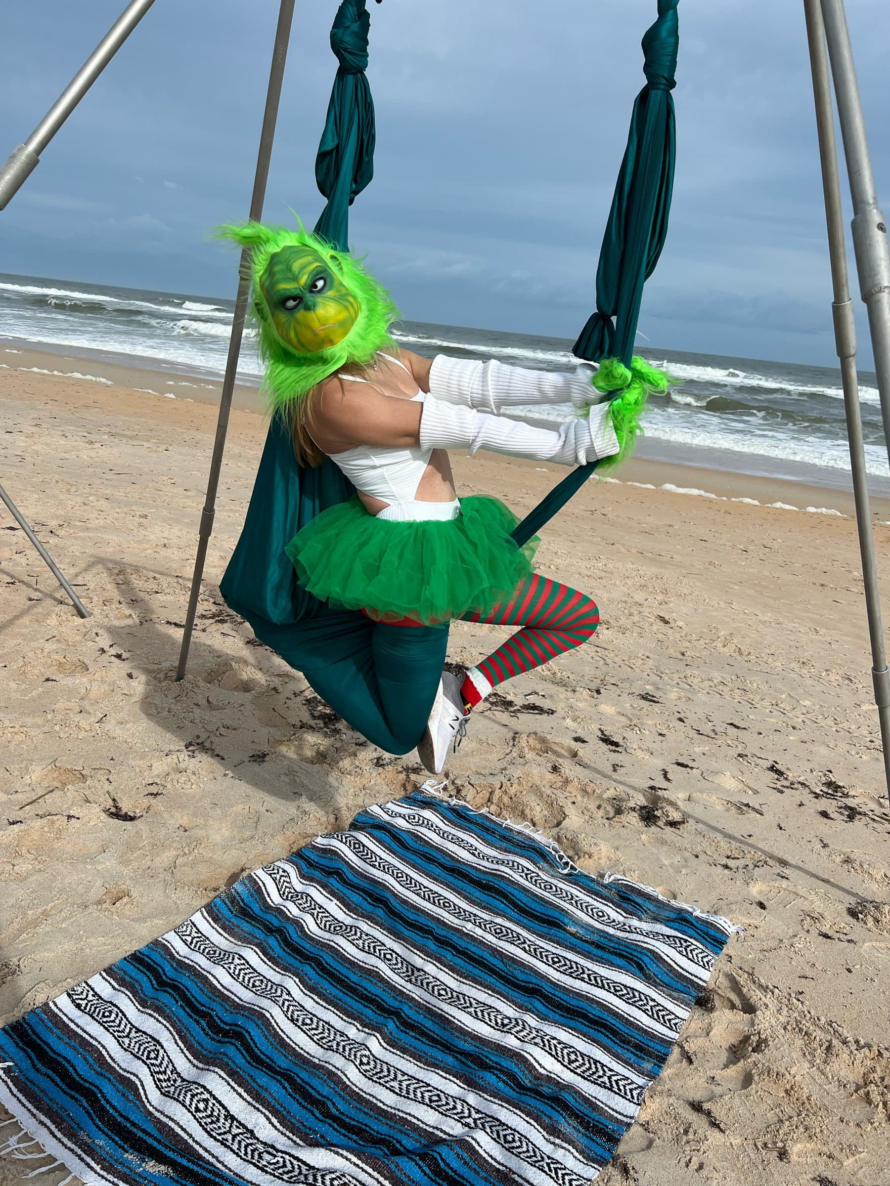 An aerial student in a green holiday costume and tutu posing in a hammock on the beach
