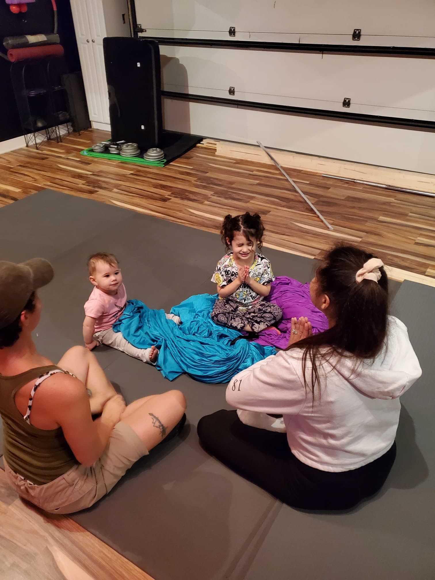 Two moms and their little ones playing with aerial fabric on the studio mats
