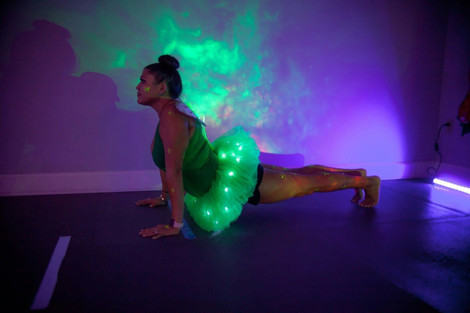 Yassy in a light-up green tutu holding a plank under green and purple lights