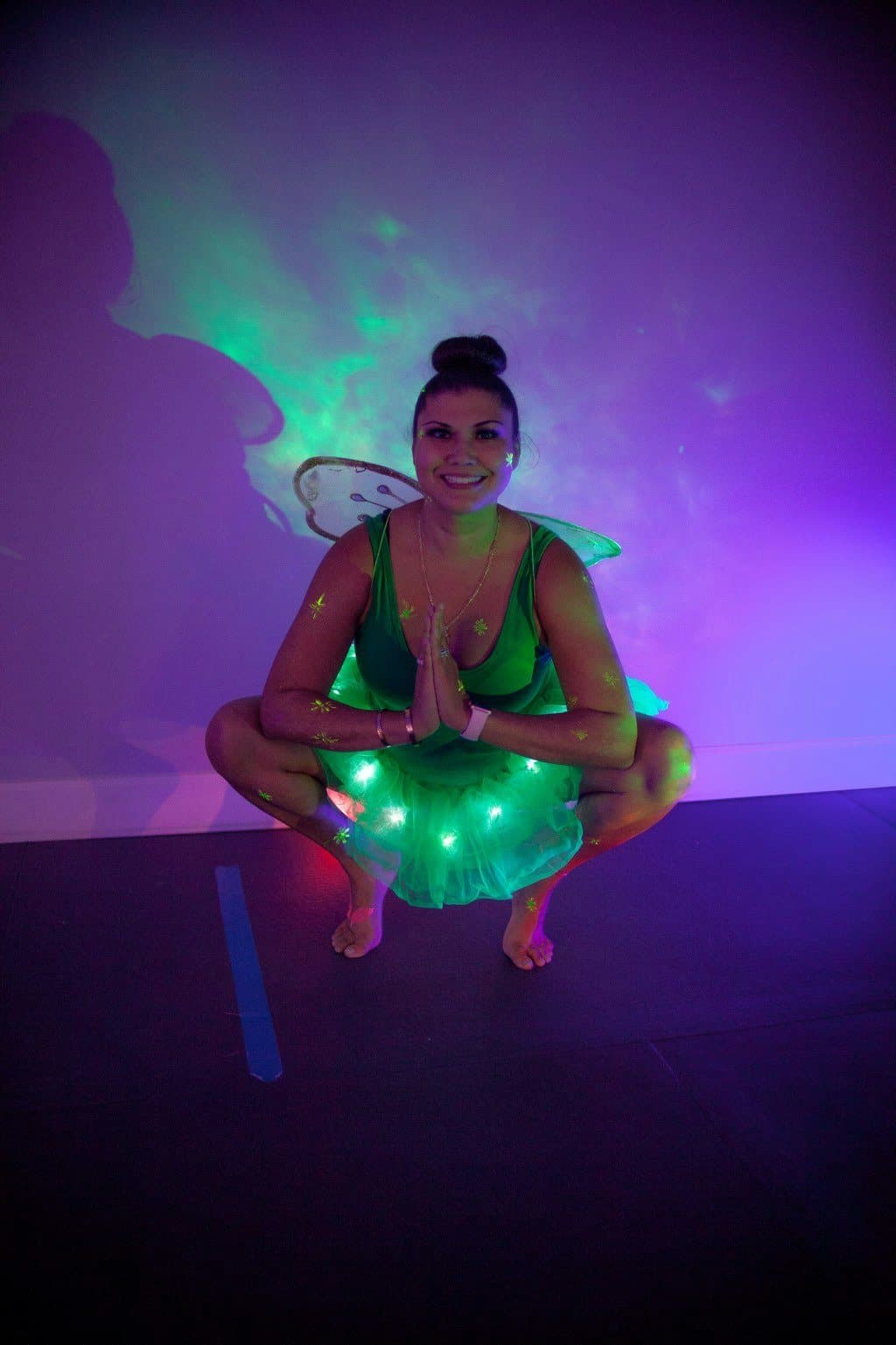 Yassy in a glowing green fairy costume, crouched in a calm pose under neon light